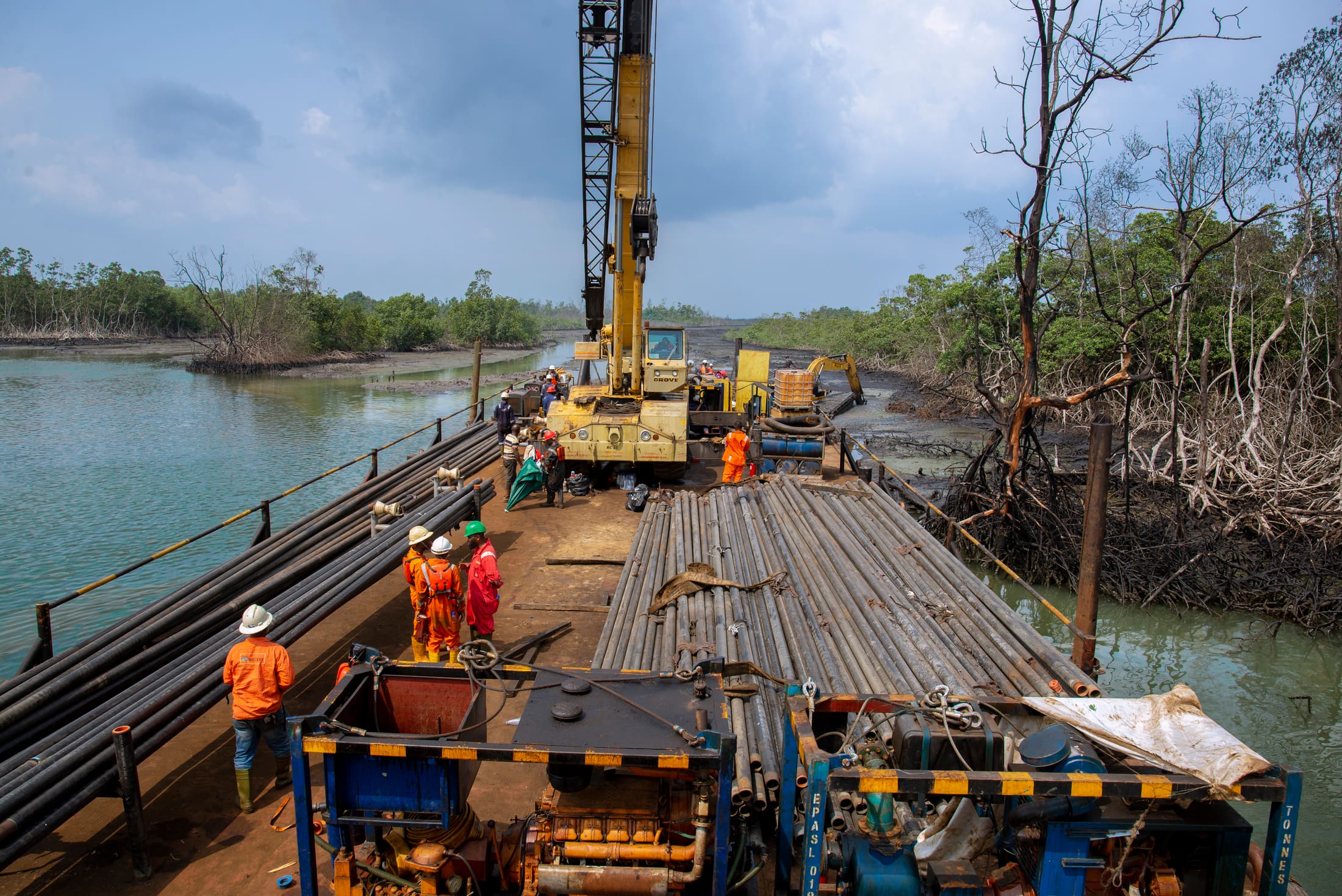 Crew and crane working a pipe-laying barge deck in the mangroves