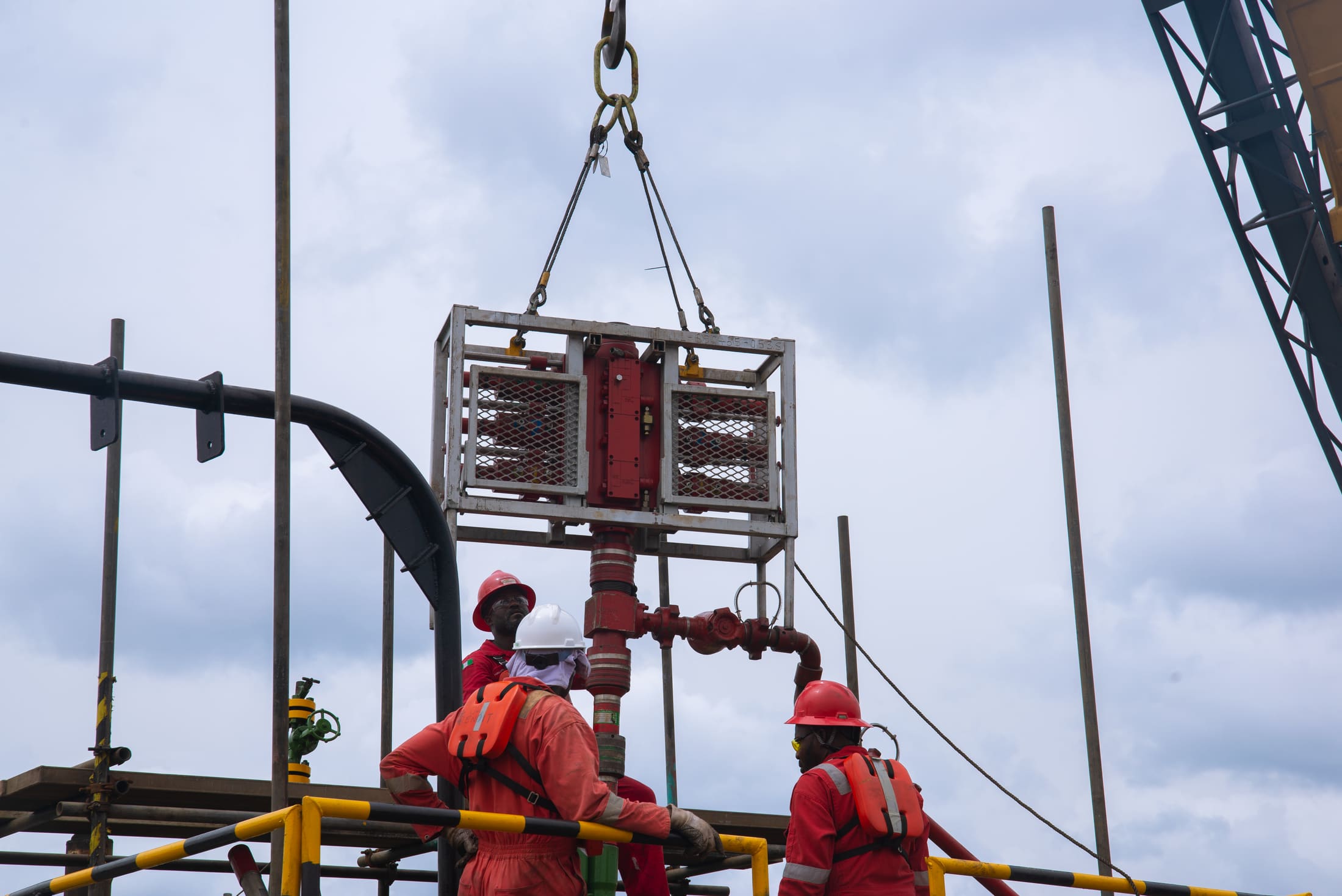 Crew guiding a valve assembly as it is lowered onto a live wellhead