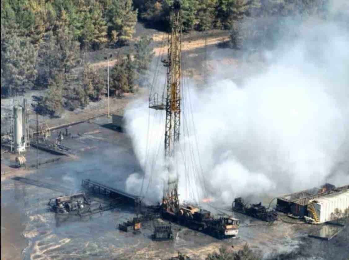 Aerial view of a drilling rig with heavy white smoke rising during a well control event