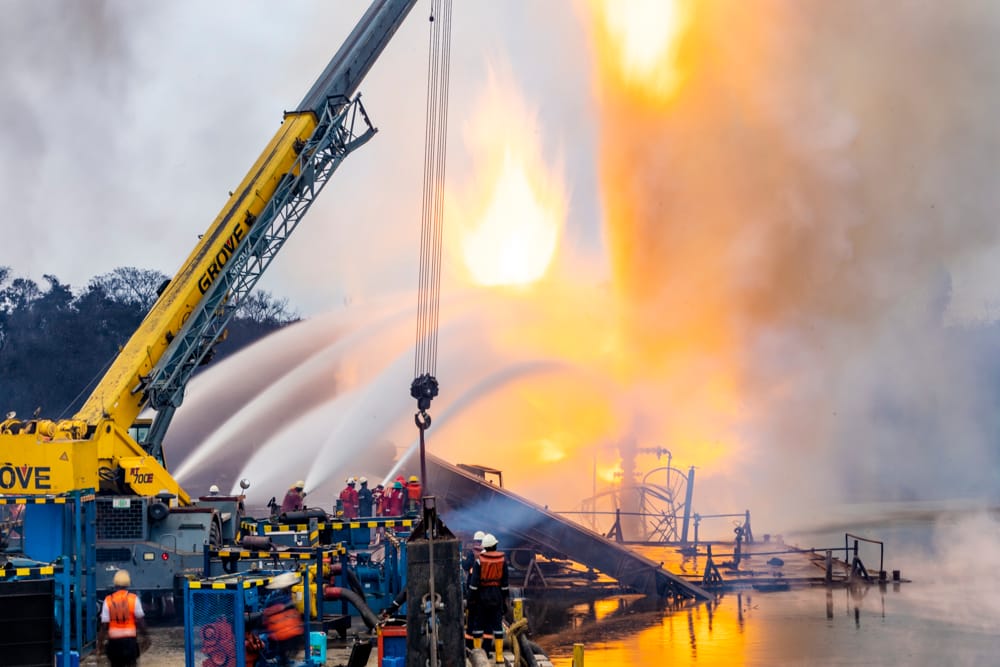 Close view of a crane boom and hose lines against an active flare