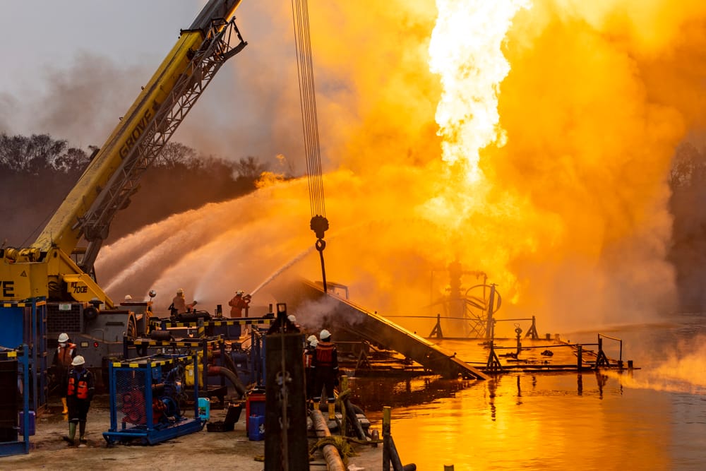 Crew directing water onto a wellsite fire beside a mobile crane