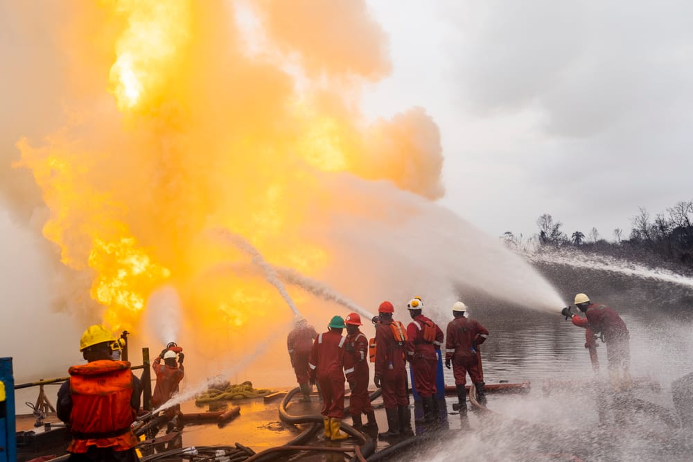A firefighting crew directing multiple hose lines onto a wellsite fire